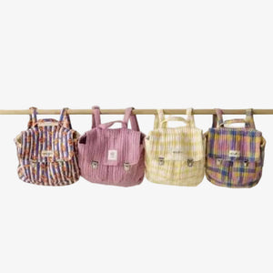 Four small striped and plaid backpacks hanging from a wooden rod against a plain light beige wall.