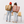 Two children seen from behind holding hands and wearing large canvas backpacks, one tan and one dusty pink, with the brand names 'GRATYI' and 'CAPRISI' printed on the back, standing in front of yellow chairs against a white studio background.