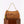 A tan woven fringe handbag with a gold chain handle and a green beaded tassel charm, displayed on a brown wooden pedestal against a white background.