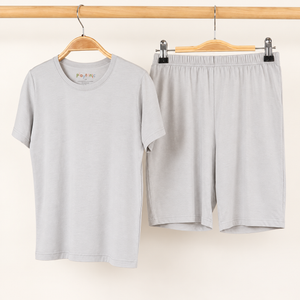 A light gray short-sleeve crewneck t-shirt and matching light gray shorts hanging on wooden hangers from a wooden clothes rack against a plain off-white background.