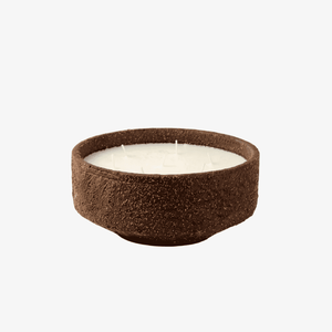 A single-wick soy candle in a textured, rustic dark brown ceramic bowl with white wax, set against a plain white background.